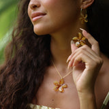 woman with brown hair wearing yellow glass plumeria necklace and earrings 