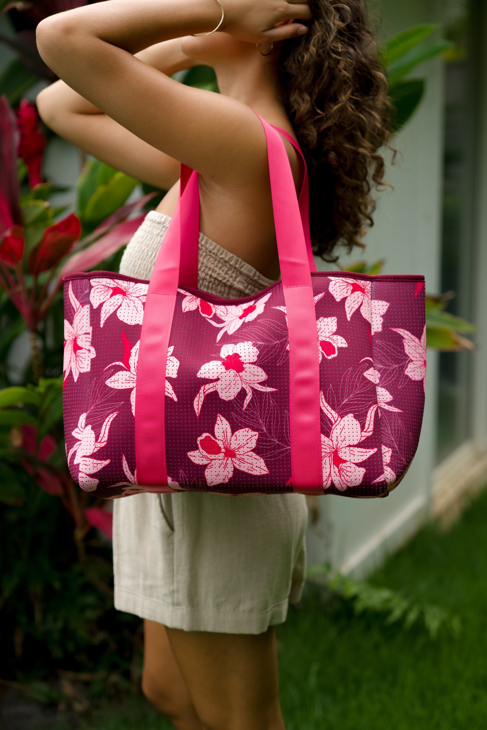 woman carrying wine colored neoprene tote bag with thick straps and detachable pouch with orchid print
