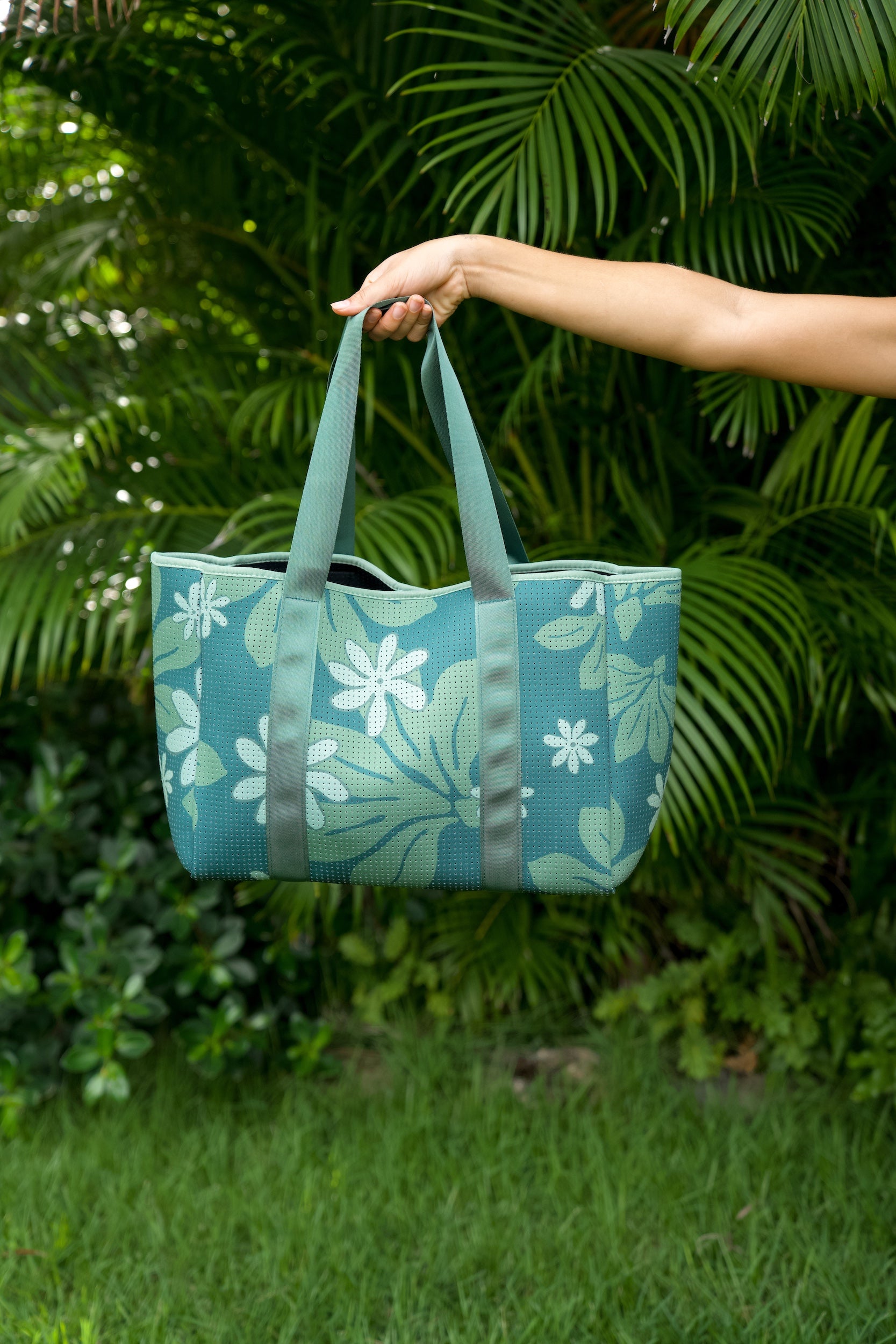 woman carrying canopy green colored neoprene tote bag with thick straps and detachable pouch with naupaka print