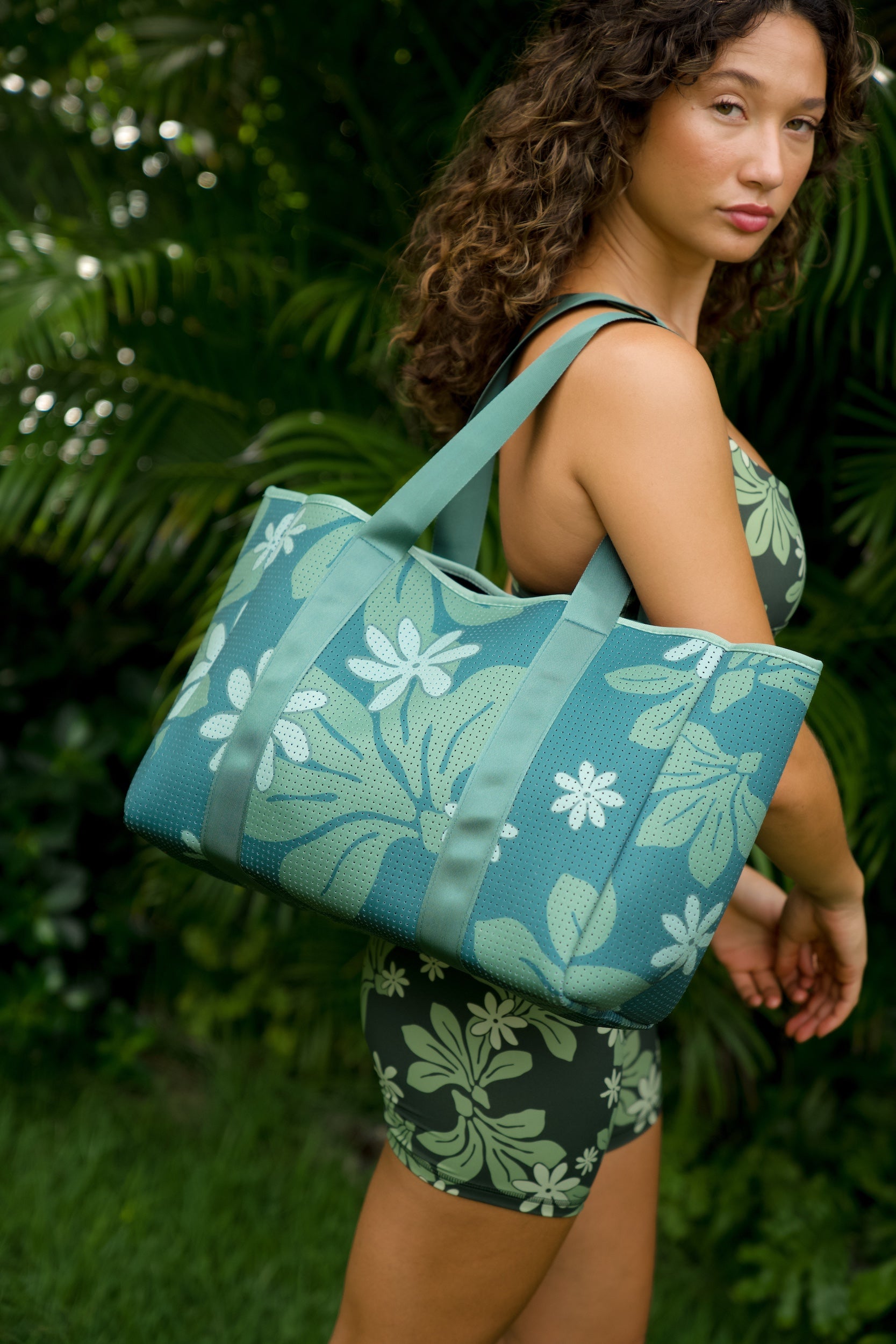 woman carrying canopy green colored neoprene tote bag with thick straps and detachable pouch with naupaka print