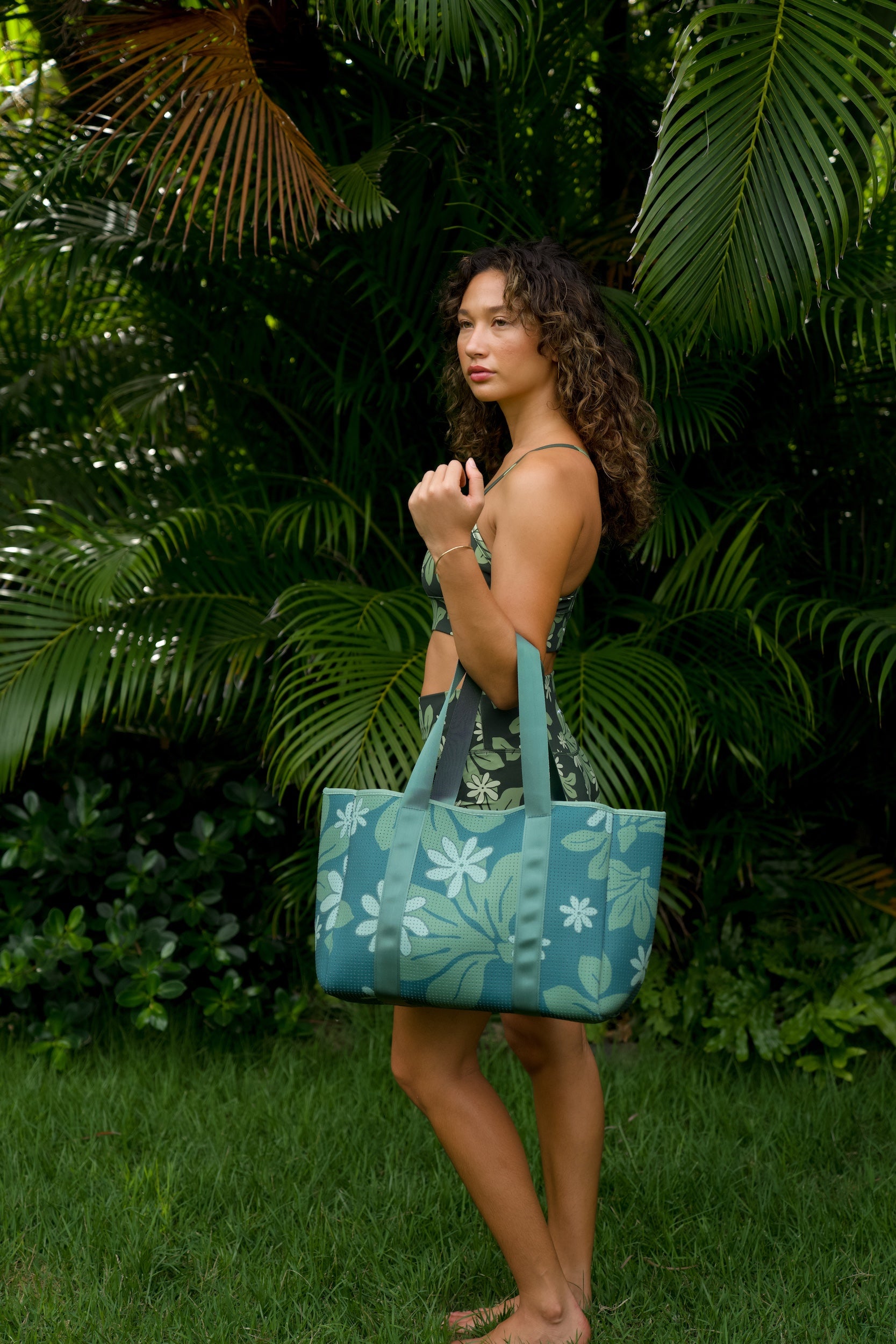 woman carrying canopy green colored neoprene tote bag with thick straps and detachable pouch with naupaka print