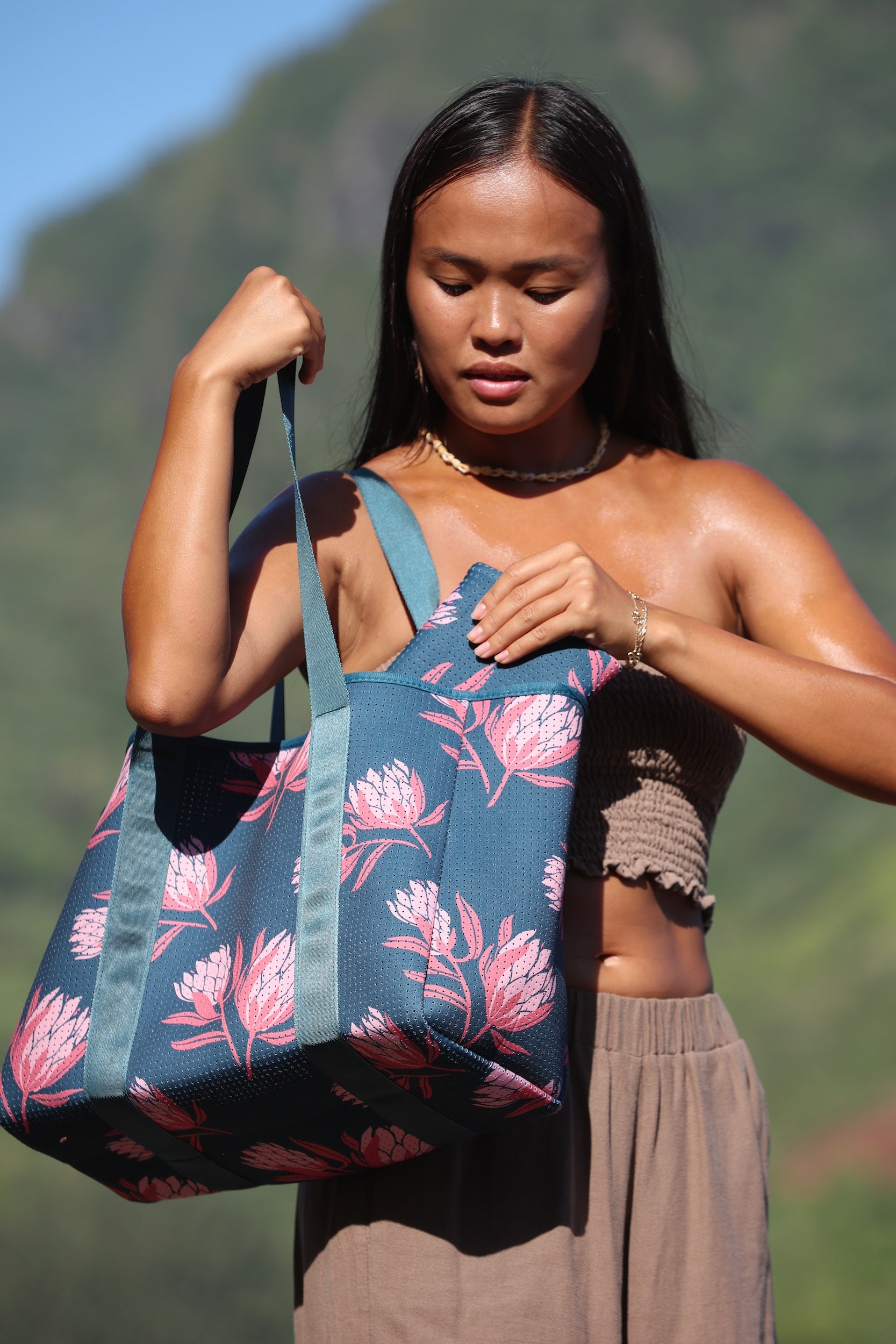 woman carrying a rich teal neoprene tote with blush colored protea print