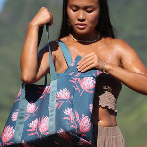 woman carrying a rich teal neoprene tote with blush colored protea print