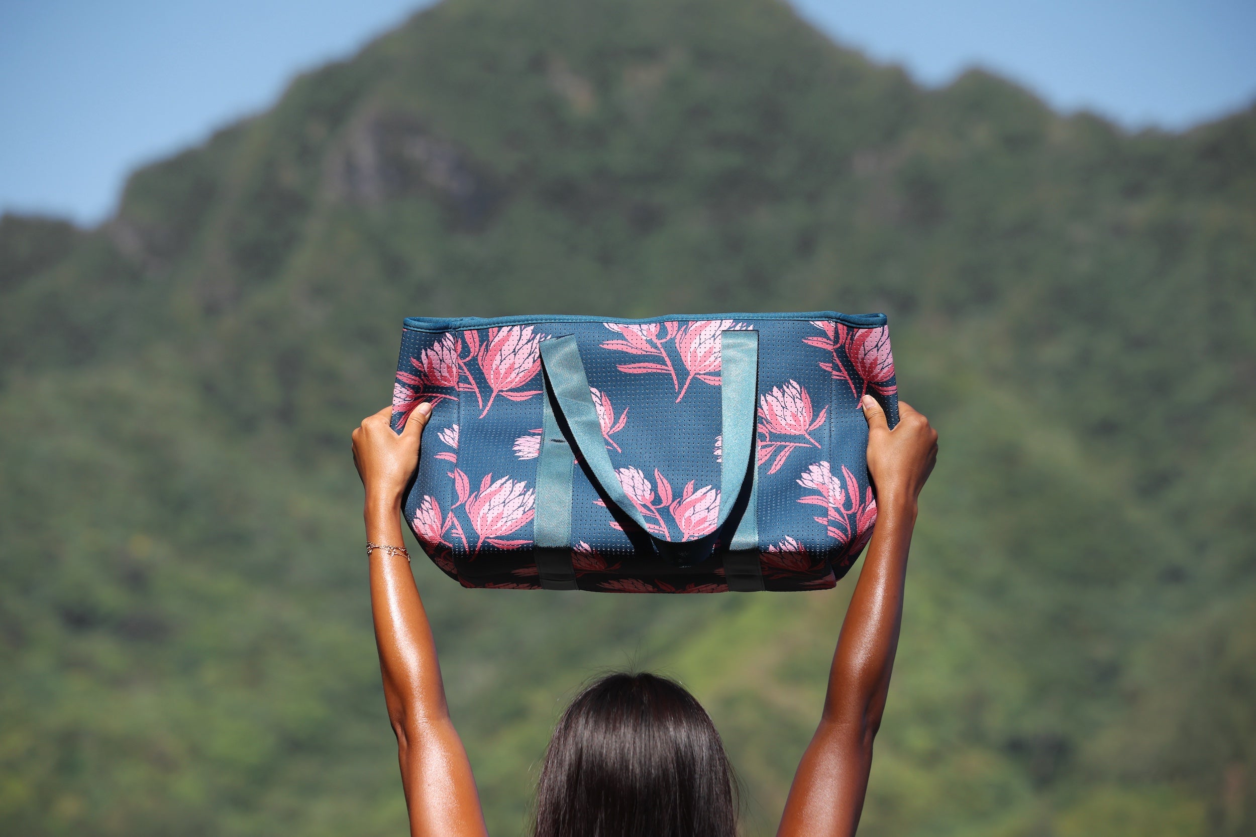 woman carrying a rich teal neoprene tote with blush colored protea print