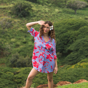 woman with brown hair wearing a mid length button up dress with periwinkle background and bright red hibiscus print.