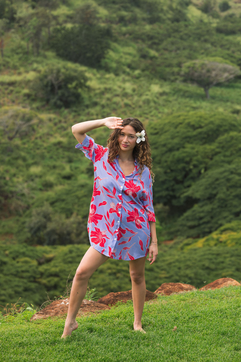 woman with brown hair wearing a mid length button up dress with periwinkle background and bright red hibiscus print.