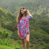 woman with brown hair wearing a mid length button up dress with periwinkle background and bright red hibiscus print.