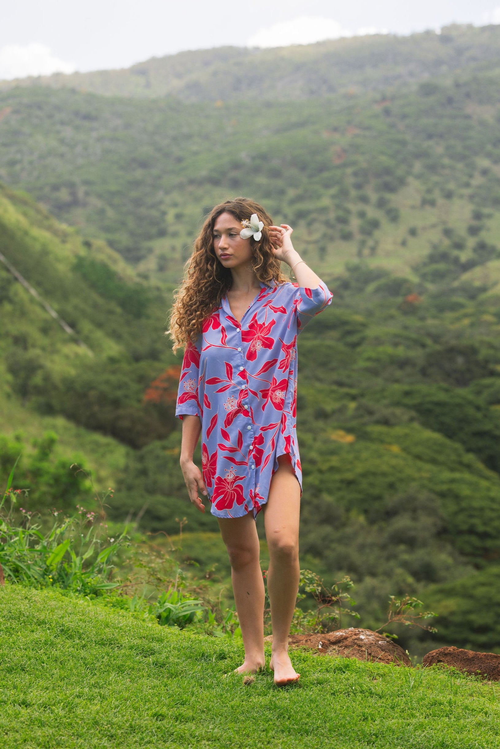 woman with brown hair wearing a mid length button up dress with periwinkle background and bright red hibiscus print.