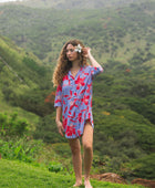woman with brown hair wearing a mid length button up dress with periwinkle background and bright red hibiscus print.