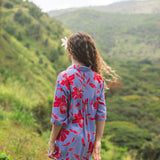 woman with brown hair wearing a mid length button up dress with periwinkle background and bright red hibiscus print.