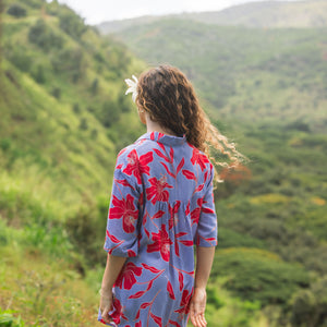 woman with brown hair wearing a mid length button up dress with periwinkle background and bright red hibiscus print.