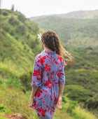 woman with brown hair wearing a mid length button up dress with periwinkle background and bright red hibiscus print.