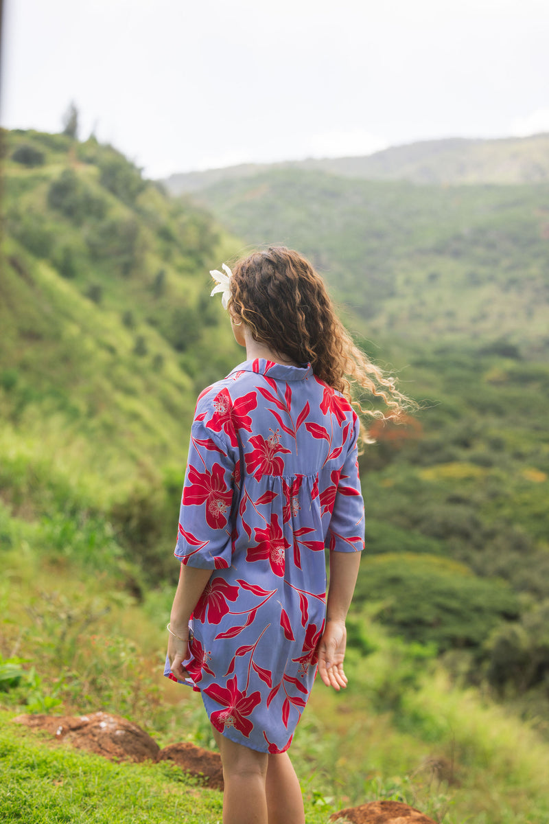 woman with brown hair wearing a mid length button up dress with periwinkle background and bright red hibiscus print.