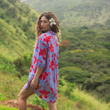 woman with brown hair wearing a mid length button up dress with periwinkle background and bright red hibiscus print.