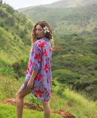 woman with brown hair wearing a mid length button up dress with periwinkle background and bright red hibiscus print.