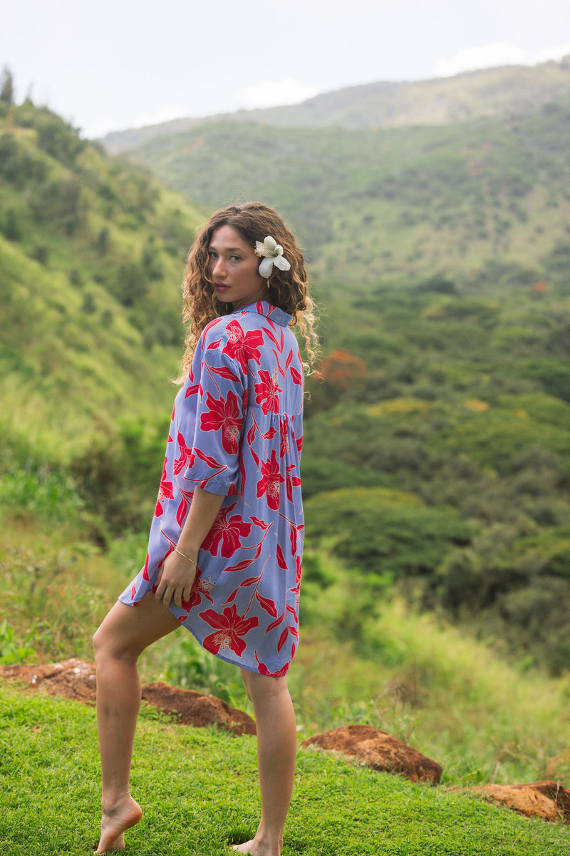 woman with brown hair wearing a mid length button up dress with periwinkle background and bright red hibiscus print.
