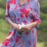 woman with brown hair wearing a mid length button up dress with periwinkle background and bright red hibiscus print.