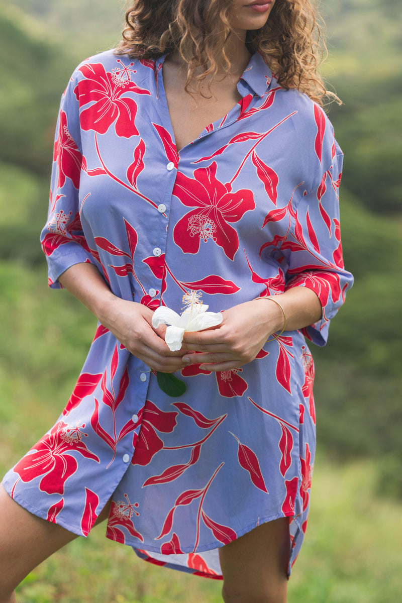 woman with brown hair wearing a mid length button up dress with periwinkle background and bright red hibiscus print.