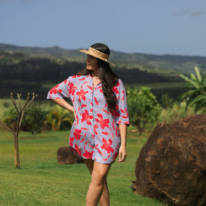 woman with brown hair wearing a mid length button up dress with periwinkle background and bright red hibiscus print.