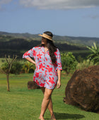 woman with brown hair wearing a mid length button up dress with periwinkle background and bright red hibiscus print.