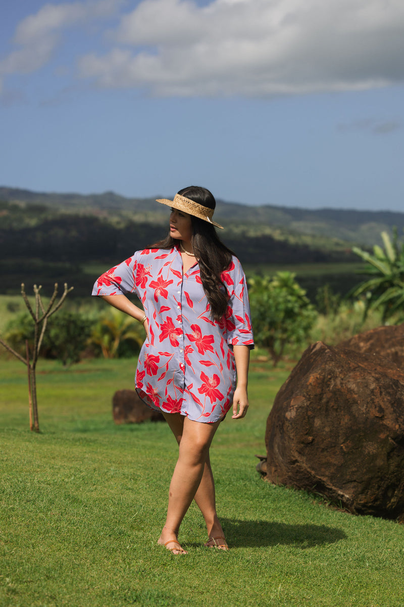 woman with brown hair wearing a mid length button up dress with periwinkle background and bright red hibiscus print.