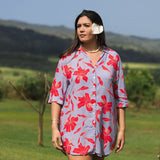 woman with brown hair wearing a mid length button up dress with periwinkle background and bright red hibiscus print.