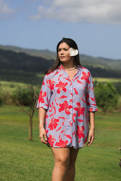 woman with brown hair wearing a mid length button up dress with periwinkle background and bright red hibiscus print.