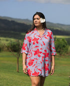 woman with brown hair wearing a mid length button up dress with periwinkle background and bright red hibiscus print.