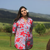 woman with brown hair wearing a mid length button up dress with periwinkle background and bright red hibiscus print.