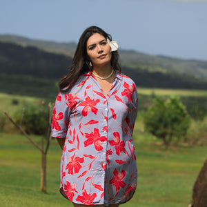 woman with brown hair wearing a mid length button up dress with periwinkle background and bright red hibiscus print.