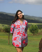woman with brown hair wearing a mid length button up dress with periwinkle background and bright red hibiscus print.