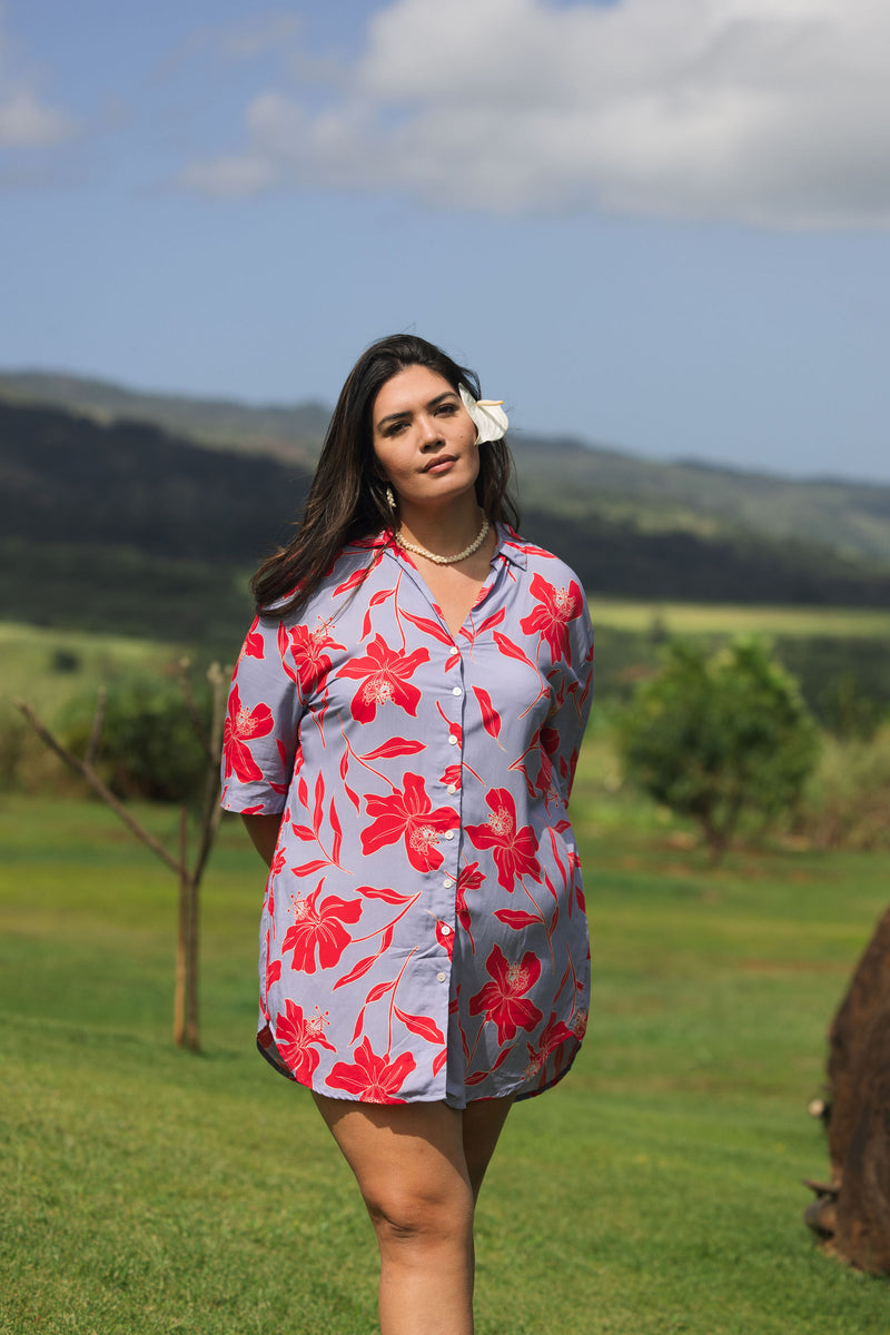 woman with brown hair wearing a mid length button up dress with periwinkle background and bright red hibiscus print.