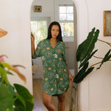 woman with brown hair wearing lush green button up dress with mid length sleeves and puakenikeni print