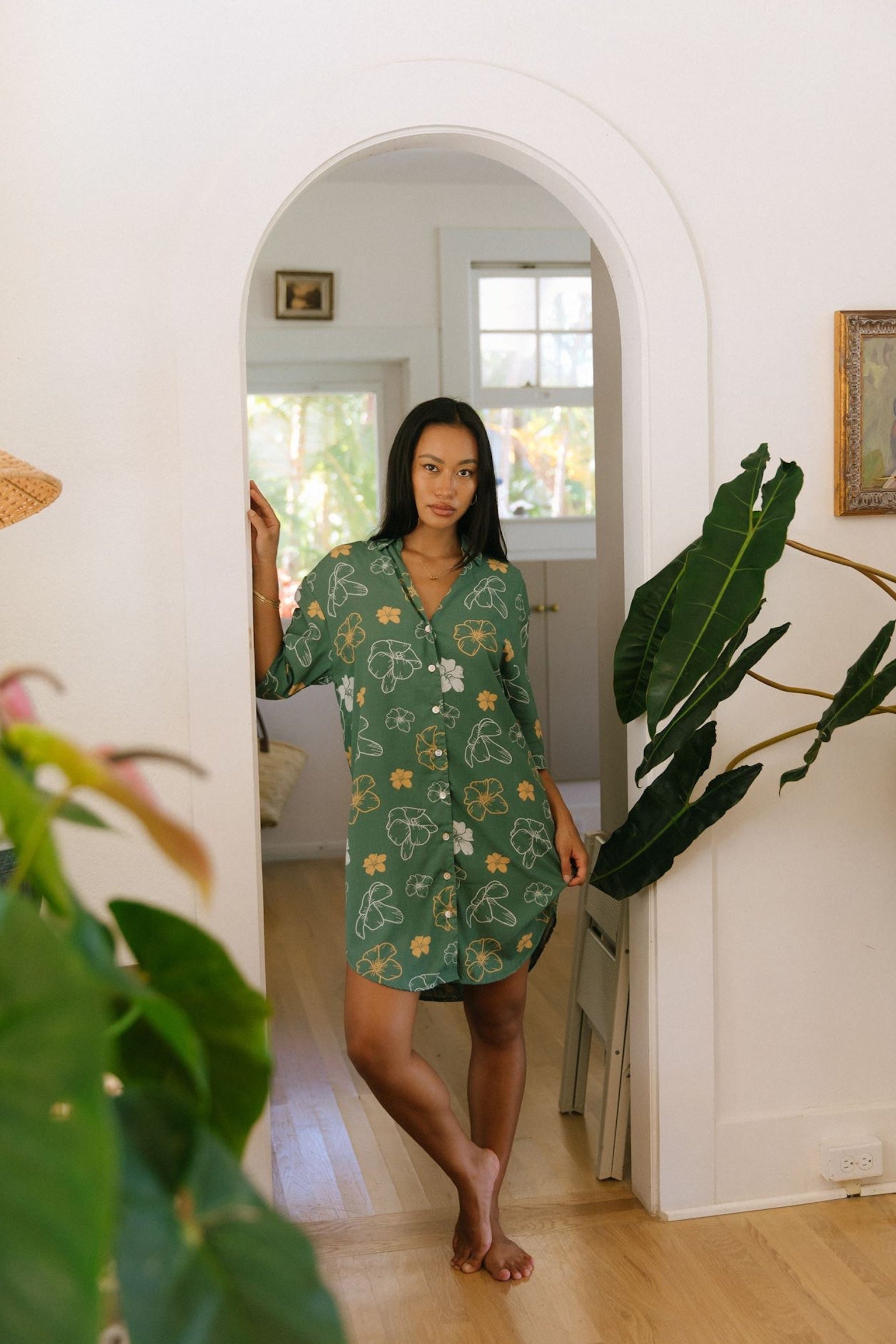 woman with brown hair wearing lush green button up dress with mid length sleeves and puakenikeni print