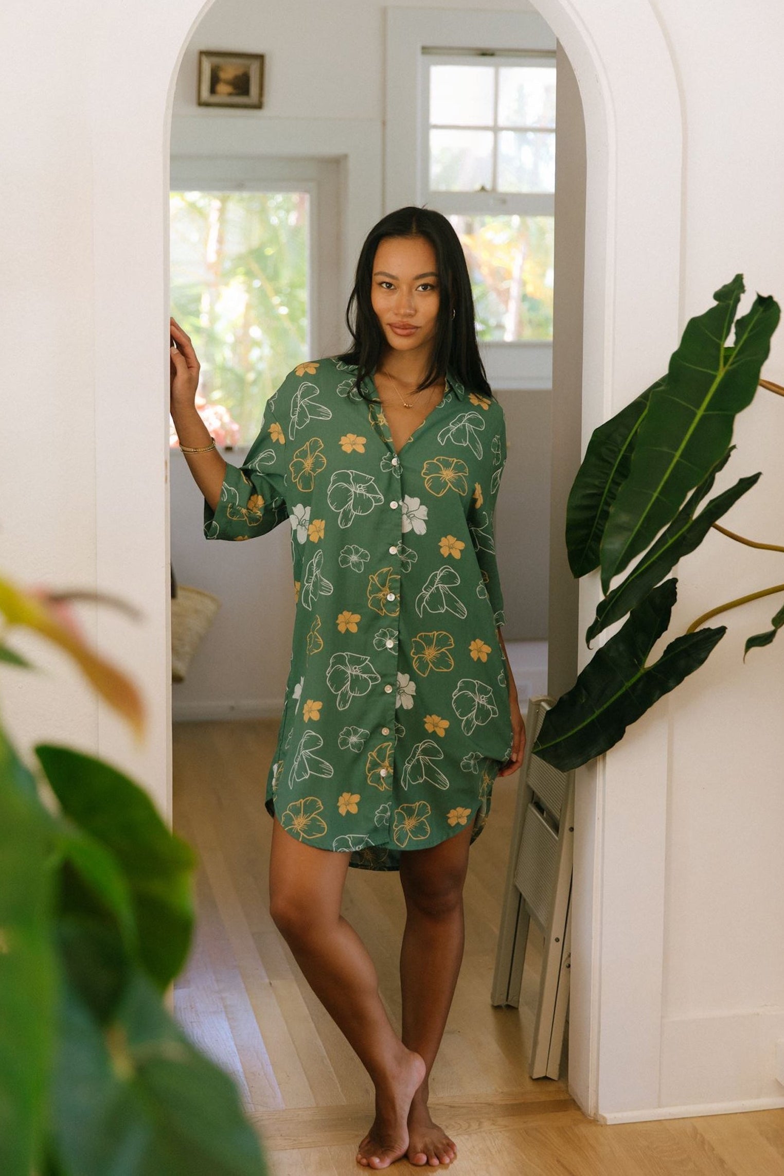 woman with brown hair wearing lush green button up dress with mid length sleeves and puakenikeni print