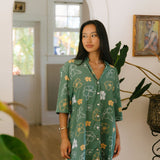 woman with brown hair wearing lush green button up dress with mid length sleeves and puakenikeni print
