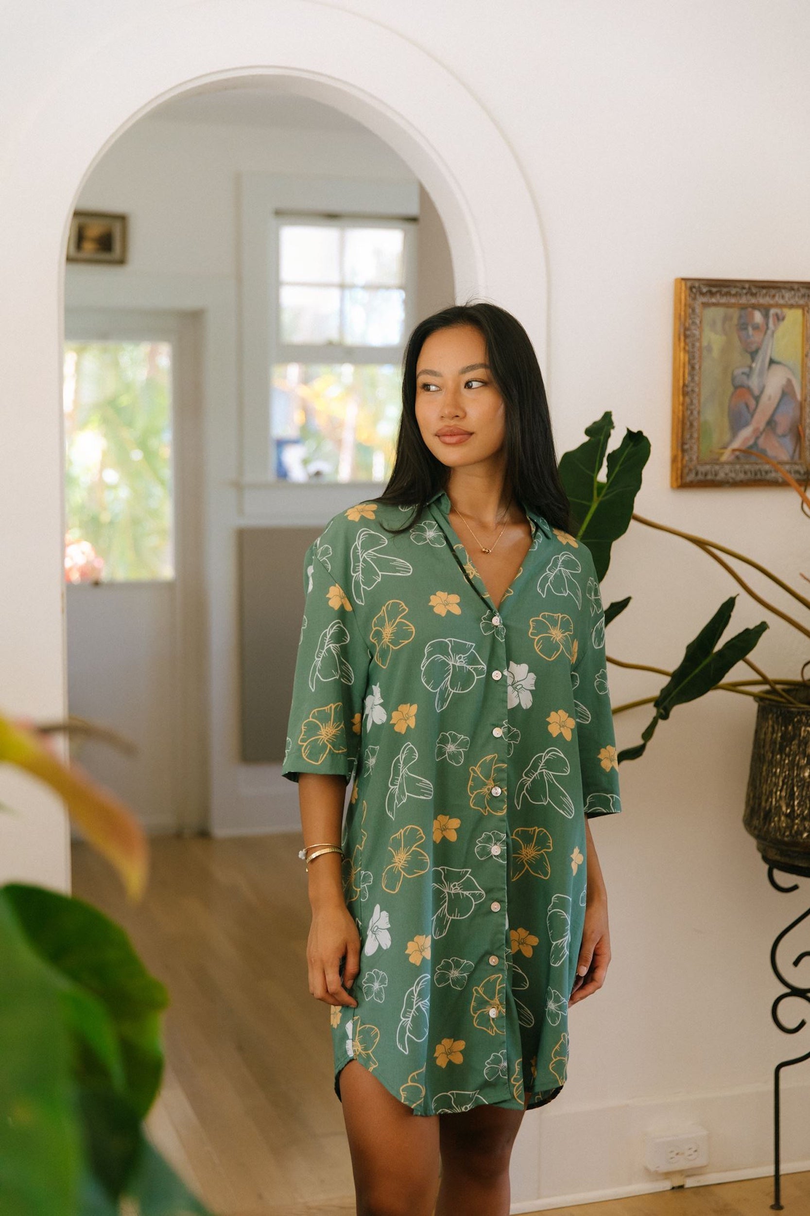 woman with brown hair wearing lush green button up dress with mid length sleeves and puakenikeni print