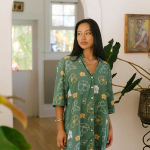woman with brown hair wearing lush green button up dress with mid length sleeves and puakenikeni print
