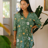 woman with brown hair wearing lush green button up dress with mid length sleeves and puakenikeni print