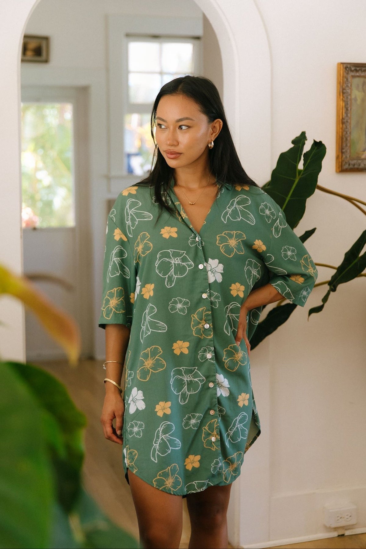 woman with brown hair wearing lush green button up dress with mid length sleeves and puakenikeni print