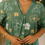 woman with brown hair wearing lush green button up dress with mid length sleeves and puakenikeni print