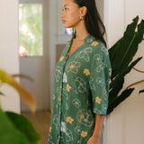woman with brown hair wearing lush green button up dress with mid length sleeves and puakenikeni print