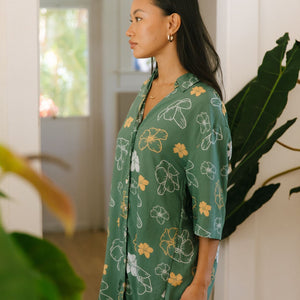woman with brown hair wearing lush green button up dress with mid length sleeves and puakenikeni print