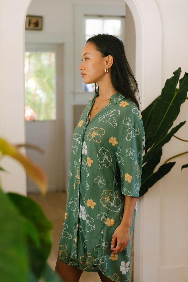 woman with brown hair wearing lush green button up dress with mid length sleeves and puakenikeni print
