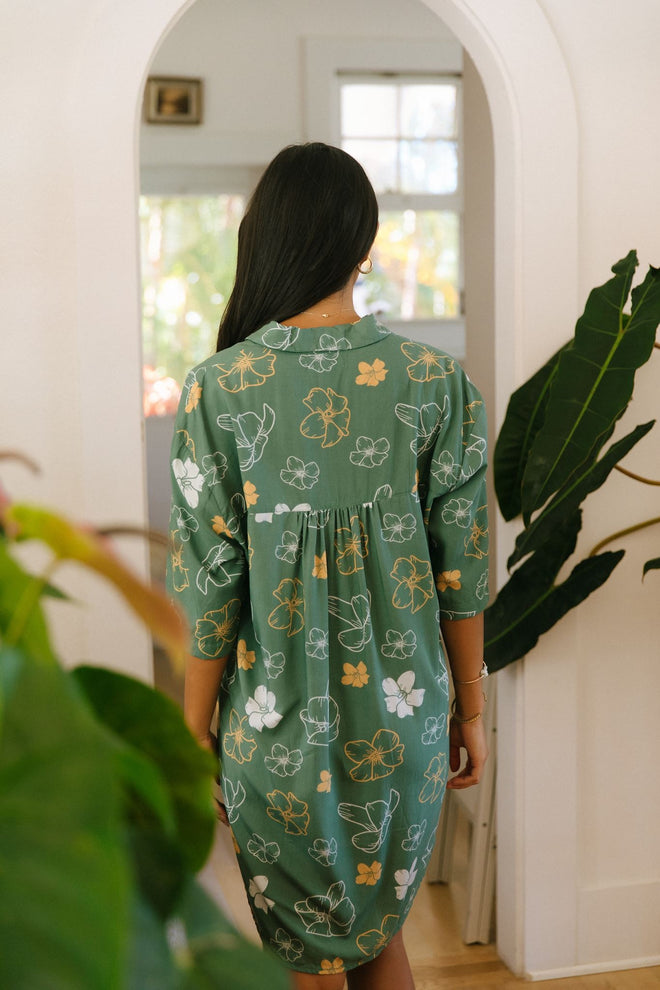 woman with brown hair wearing lush green button up dress with mid length sleeves and puakenikeni print