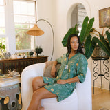 woman with brown hair wearing lush green button up dress with mid length sleeves and puakenikeni print