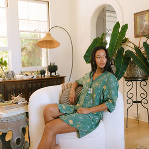 woman with brown hair wearing lush green button up dress with mid length sleeves and puakenikeni print