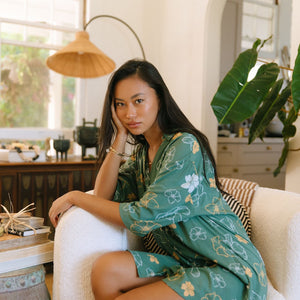 woman with brown hair wearing lush green button up dress with mid length sleeves and puakenikeni print