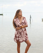 Woman with brown hair wearing a button up dress in blush and brown hibiscus print