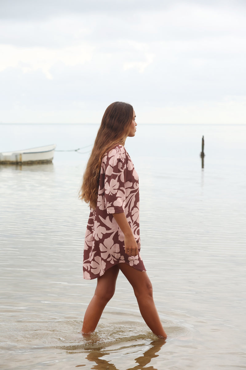 Woman with brown hair wearing a button up dress in blush and brown hibiscus print